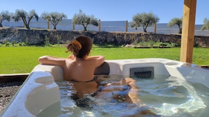 Eine Person entspannt sich in einem Whirlpool im Freien, mit einer Rasenfläche und Bäumen im Hintergrund.