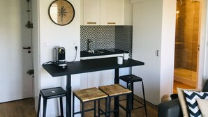 A compact kitchen with a black countertop, a built-in stove, and a patterned backsplash. There are two stools and a small table.