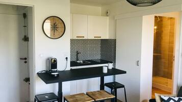 Une cuisine compacte avec un plan de travail noir, une cuisinière intégrée et un crédence décorée. On y trouve deux tabourets et une petite table.