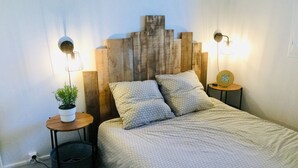 A bedroom with a wooden headboard, a bed with patterned bedding, two bedside tables with lamps, and a small potted plant.