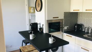 Een kleine keuken met een koffiezetapparaat, magnetron en wasmachine.