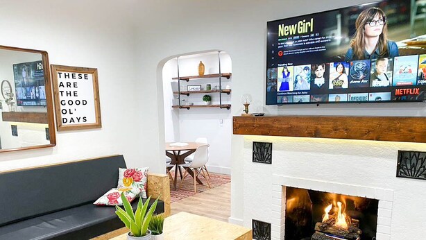 A modern living room with a fireplace, a flat-screen TV displaying a Netflix interface, a comfortable sofa, and a coffee table with plants. - Modern House, Walk To Historic Downtown! (Grants Pass)