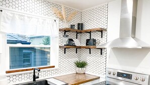 A modern kitchen with a stainless steel stove, a sink, and wooden shelves above. - Modern House, Walk To Historic Downtown! (Grants Pass)