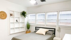A bedroom with a bed, a white shelf unit, a potted plant, and a window with blinds. - Modern House, Walk To Historic Downtown! (Grants Pass)