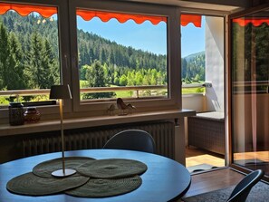 Quarto com vista para uma floresta, uma mesa com jogos americanos, um radiador e uma cadeira.