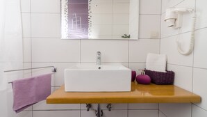 A bathroom with a white sink, a mirror, a hairdryer, and a purple towel. - Lavender Garden Apartments - Comfort Studio Apartment (Ground Floor) (Dubrovnik)