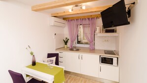 A compact kitchen with white cabinets, a built-in microwave, and a window with purple curtains. - Lavender Garden Apartments - Comfort Studio Apartment (Ground Floor) (Dubrovnik)