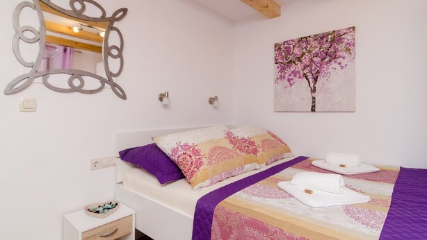Ein Schlafzimmer mit einem Bett, einem Nachttisch, einem Zier-Spiegel und einem an der Wand hängenden Gemälde.