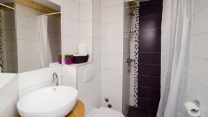 Ein modernes Badezimmer mit einem weißen Waschbecken, einer Dusche mit dunkel gefliestem Wandbereich und einem weißen Vorhang.