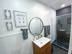 A bathroom with a sink, mirror, and a shower area. There are signs on the wall indicating bathroom procedures. - Modern Studio in the Heart of Grants Pass (Grants Pass)