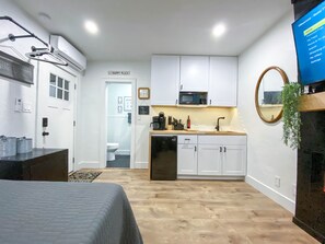 A compact hotel room with a kitchenette, a bed, a TV, and a view of the bathroom. - Modern Studio in the Heart of Grants Pass (Grants Pass)