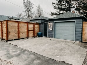 A residential garage with a grey door, a wooden fence, and a blue trash can. - Modern Studio in the Heart of Grants Pass (Grants Pass)