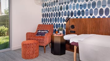 Relax in a serene space with a large window overlooking lush greenery, a comfortable armchair, and a neatly made bed.
