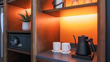 A compact kitchenette with a coffee maker, two cups, and a potted plant.