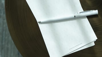 A white notepad with a geometric pattern and a pen on a round, dark wooden table.