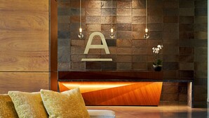 A modern reception area with a wooden reception desk, a large black pendant light, and a geometric patterned rug. - The Ameswell Hotel (Mountain View)