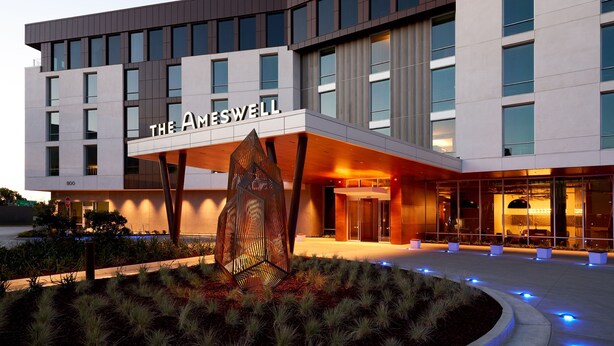 A modern hotel with a prominent entrance, large windows, and a well-lit facade. - The Ameswell Hotel (Mountain View)