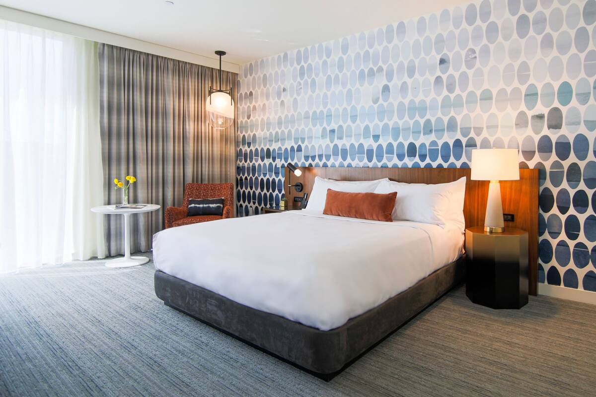 Ett modernt hotellrum med en stor säng, ett runt bord, en stol och en vägg med ett mönster.