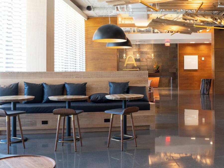 Un espacio lounge moderno con un banco largo, mesas redondas y taburetes de bar.