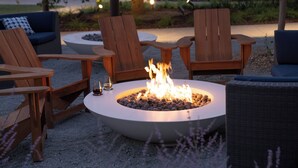 A fire pit surrounded by wooden chairs and a sofa, set on a gravel surface. - The Ameswell Hotel (Mountain View)