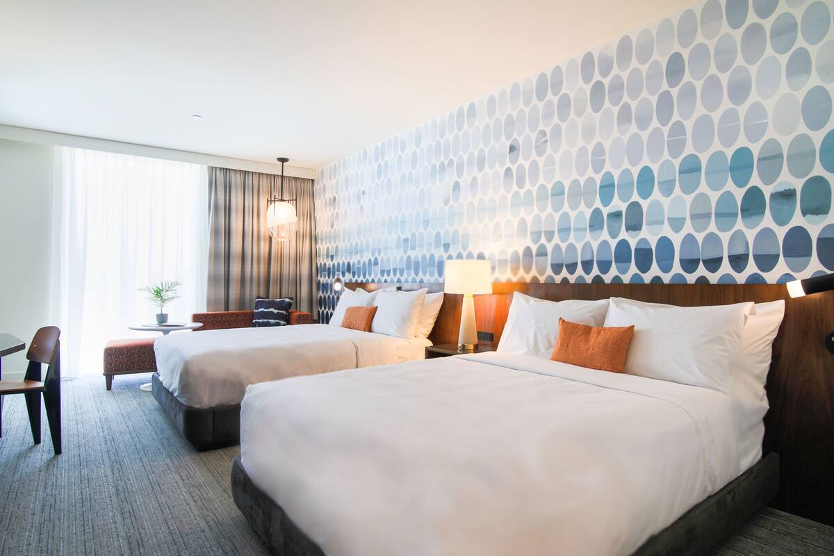 Ett hotellrum med två sängar, ett skrivbord, en stol, en lampa och utsikt över omgivningarna.