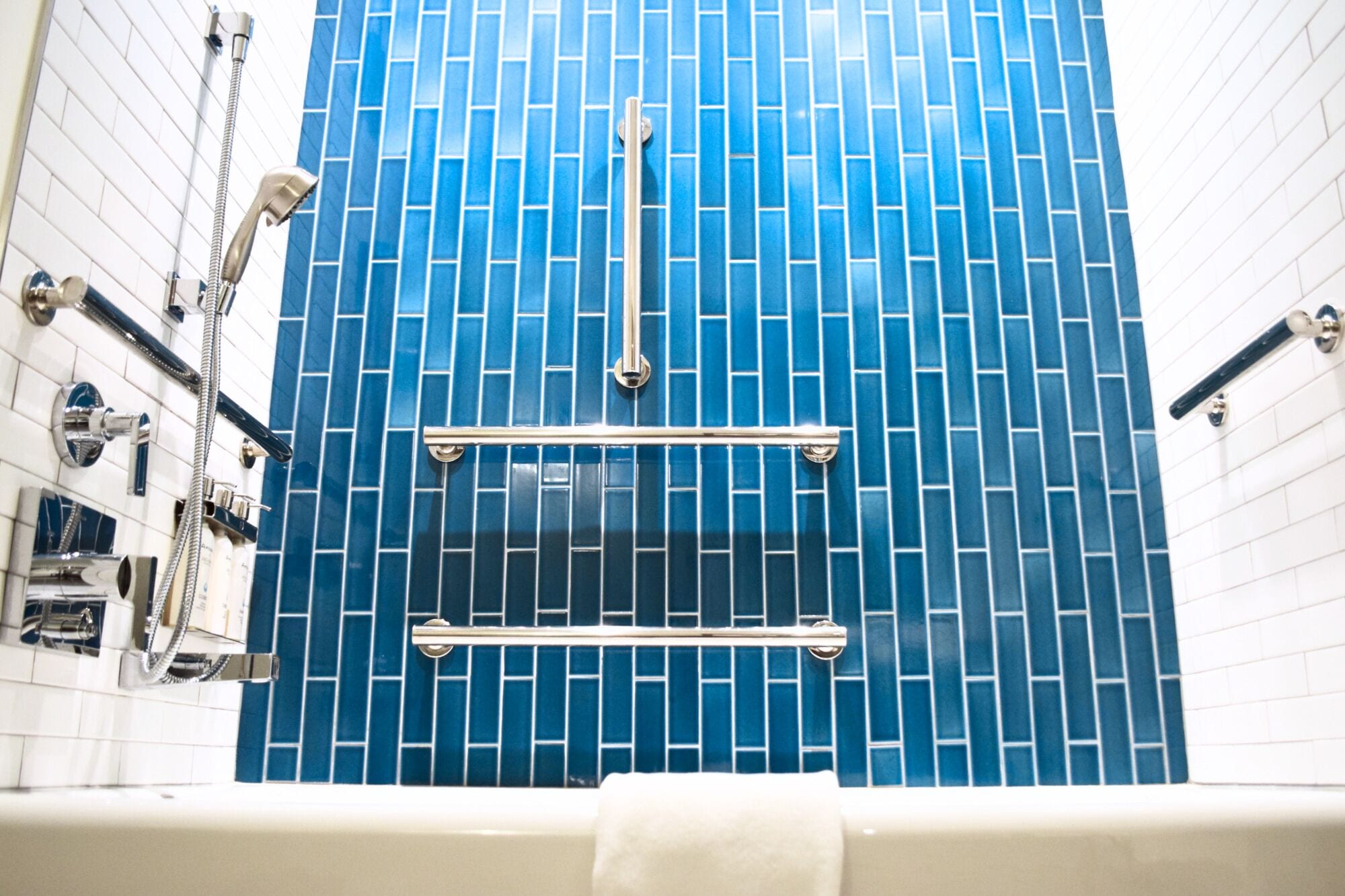 A bathroom with blue tiled walls, a white bathtub, and a shower with a handheld showerhead.