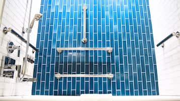 A bathroom with blue tiled walls, a white bathtub, and a shower with a handheld showerhead.