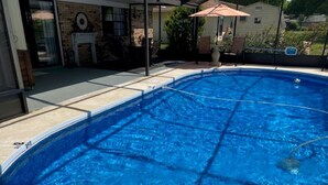 Una piscina con un borde empedrado, una zona de patio con mobiliario exterior y un muro de ladrillo al fondo.