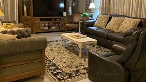 Una sala de estar con un televisor grande, un mueble de madera para equipo multimedia, dos sofás, una mesa de centro y una alfombra estampada.