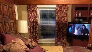 Un dormitorio con cama, televisor y ventana con cortinas.