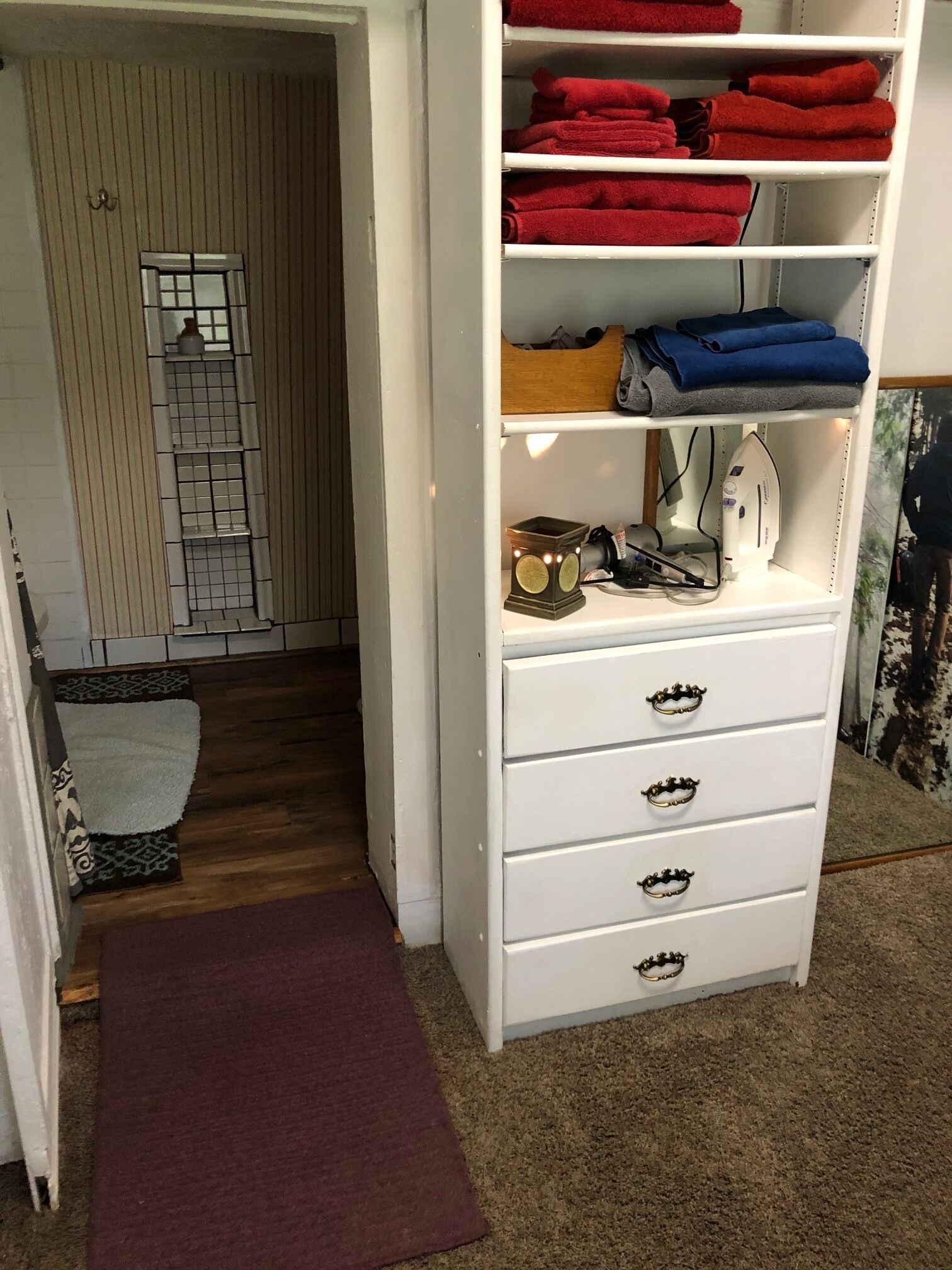 A room with a white wardrobe, a red and blue towel rack, a small mirror, and a wooden ladder.