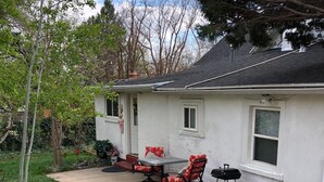 Una casa con un patio que tiene una mesa, sillas, una parrilla y un pequeño jardín con rocas y plantas.