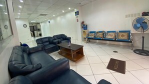 Een receptiegedeelte met leren banken, een salontafel, een blauwe bank met kussens, een ventilator en een welkomstmat.