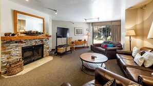 Ein Wohnzimmer mit Kamin aus Stein, Ledersofas, einem Fernseher und einem großen Fenster mit Vorhängen.