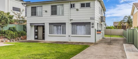 A two-story residential building with a front yard, a gated driveway, and a sign indicating holiday rental availability.