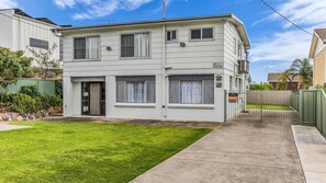 A two-story residential building with a front yard, a gated driveway, and a sign indicating holiday rental availability. - Fishos Hangout 1 - Unit 1 Sinclair St 21 (BERMAGUI)