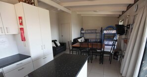 Uma cozinha compacta com armários brancos, bancada preta e uma área de refeições com mesa e cadeiras.