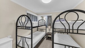 A room with three bunk beds, a bedside table with a lamp, and a window with curtains. - Fishos Hangout 2 - Unit 2 Sinclair St 21 (BERMAGUI)