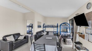 A room with bunk beds, a sofa, a table, chairs, a TV, and a bulletin board. - Fishos Hangout 2 - Unit 2 Sinclair St 21 (BERMAGUI)