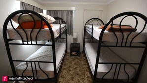 Una habitación con literas, una mesita de noche pequeña con una lámpara y una puerta al fondo.