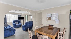 A modern living room with a dining area, featuring a flat-screen TV, blue sofas, and a wooden dining table. - Fishos Hangout 2 - Unit 2 Sinclair St 21 (BERMAGUI)