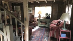 Un interior rústico con una escalera, un sofá de cuadros, una alfombra estampada y una lámpara.