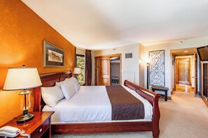 A hotel room with a large bed, a bedside table with a lamp, a wooden headboard, a framed picture on the wall, and a door leading to a hallway. - Silver King 403 | 150 Yards to Lifts | Fireplace | Kitchen | End Unit | Mtn View | Pool & Hot Tub (Park City)