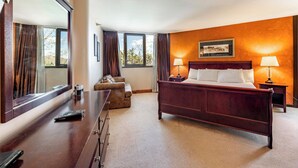 Une chambre d’hôtel avec un grand lit, un bureau avec une télécommande, une chaise et une fenêtre avec des rideaux.