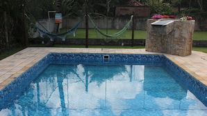 A rectangular swimming pool with blue mosaic tiles, surrounded by a stone border and a hammock. - Recanto do Vale (PIRACAIA)
