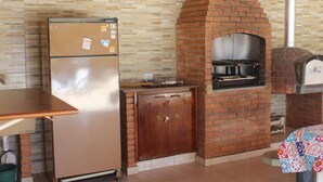 A compact kitchen with a brick oven, a refrigerator, and a wooden cabinet. - Recanto do Vale (PIRACAIA)