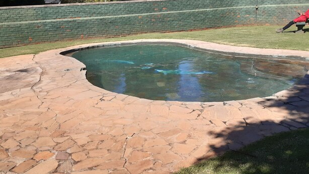 Une piscine avec une terrasse en pierre et un mur de briques en arrière-plan.