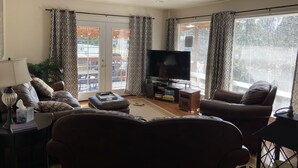 Een woonkamer met een bank, fauteuils, een televisie en een bijzettafeltje met een lamp en boeken.