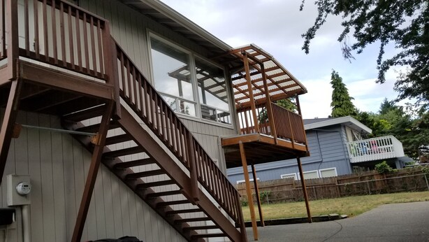 Een huis met twee verdiepingen, met een houten trap die naar een balkon leidt.