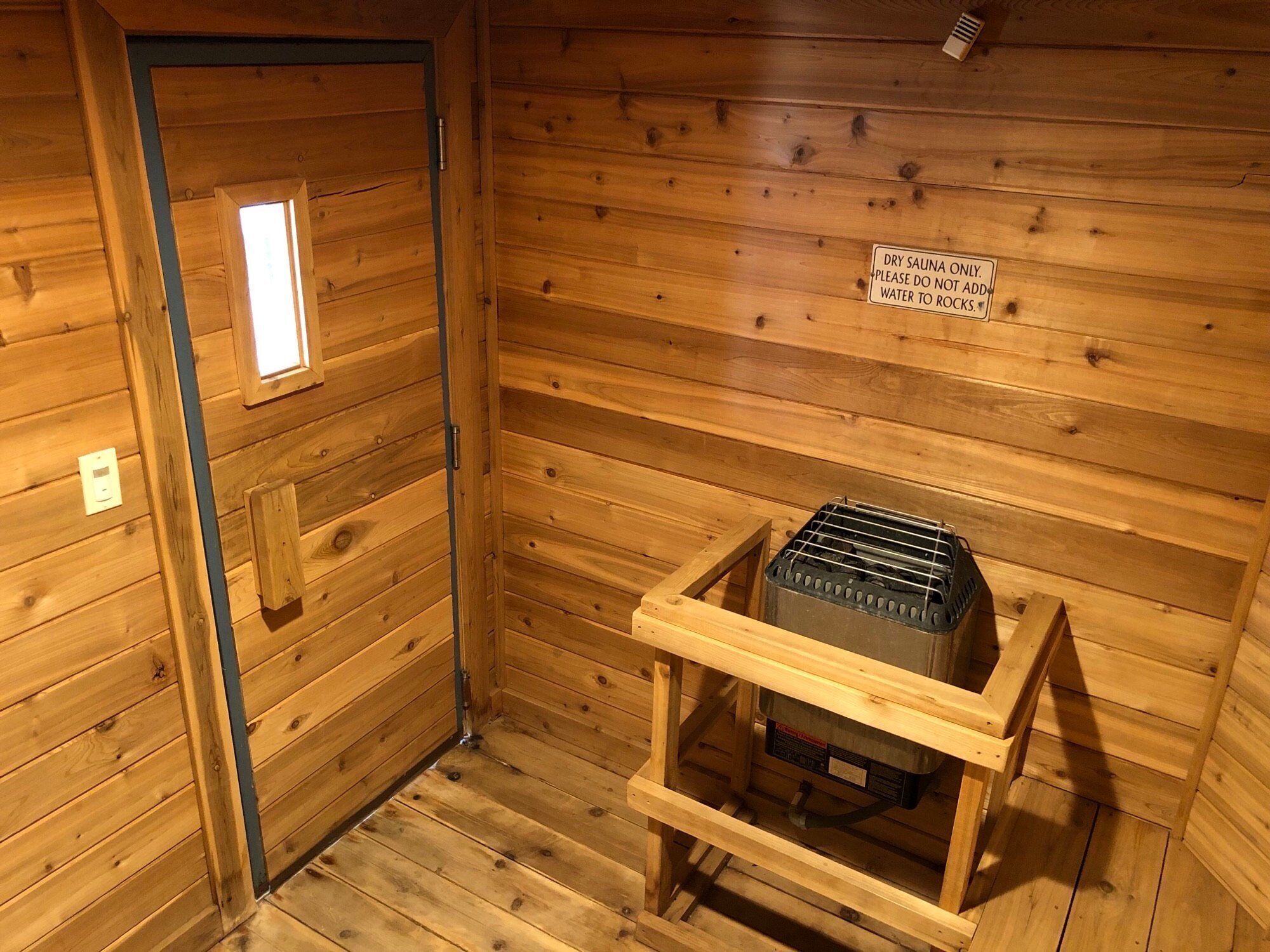 Une salle de sauna à sec avec des murs en bois et un appareil de chauffage de sauna placé sur un support en bois.